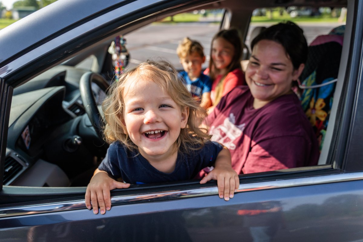 A family of four smiling together inside a car.