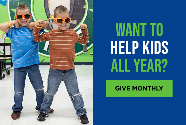 Twin boys in a school cafeteria, wearing matching orange sunglasses and holding their arms up as though flexing their muscles. A headline reads: Want to help kids all year? A button reads: Give monthly