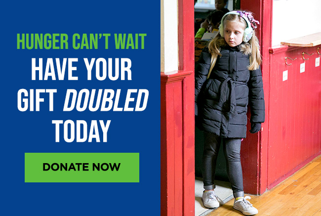 A girl dressed for winter with a serious expression on her face walking out of a classroom door. A headline reads: Hunger can’t wait. Have your gift doubled today. A button reads: Donate now.