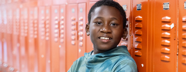 Kendrick, with his arms crossed, smiling and leaning against a row of orange lockers.