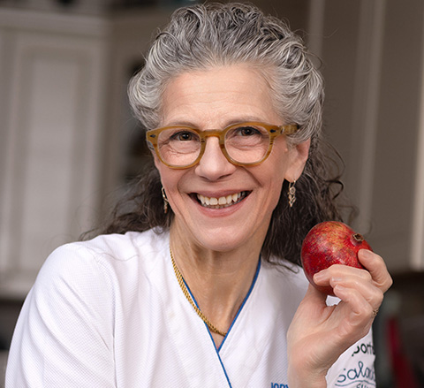 Chef Jody Adams smiling and holding a small pomegranate in one hand