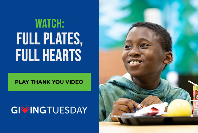 A smiling boy sitting at a table with a school lunch tray in front of him. He’s looking toward a headline reading: Watch: Full plates, full hearts. A button reads: Play thank you video. Below the button is the Giving Tuesday logo.