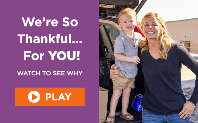 Mom Caysha standing with her arm around her toddler-aged son who is standing inside the trunk of their car. They’re both smiling. A headline reads: We’re So Thankful for you! Watch to see why. A button reads: Play