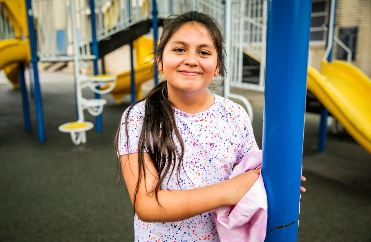 A young girl smiles brightly while standing on a colorful playground.