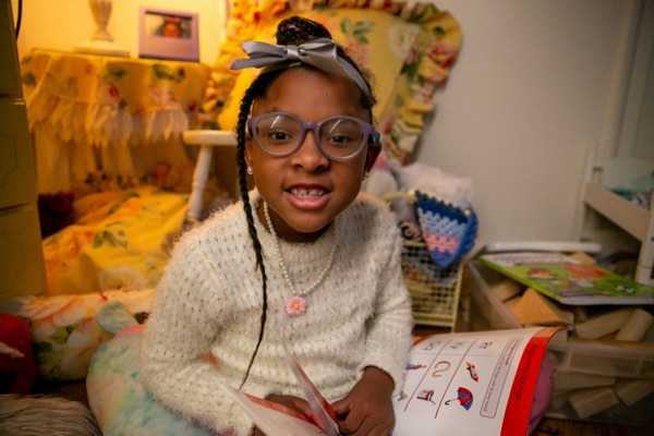 A girl holding a book smiles at the camera