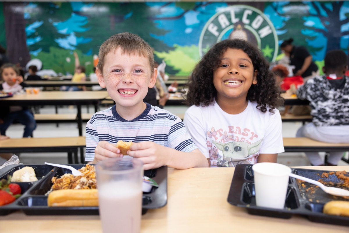 Two children sitting at a table, enjoying a meal in front of them.