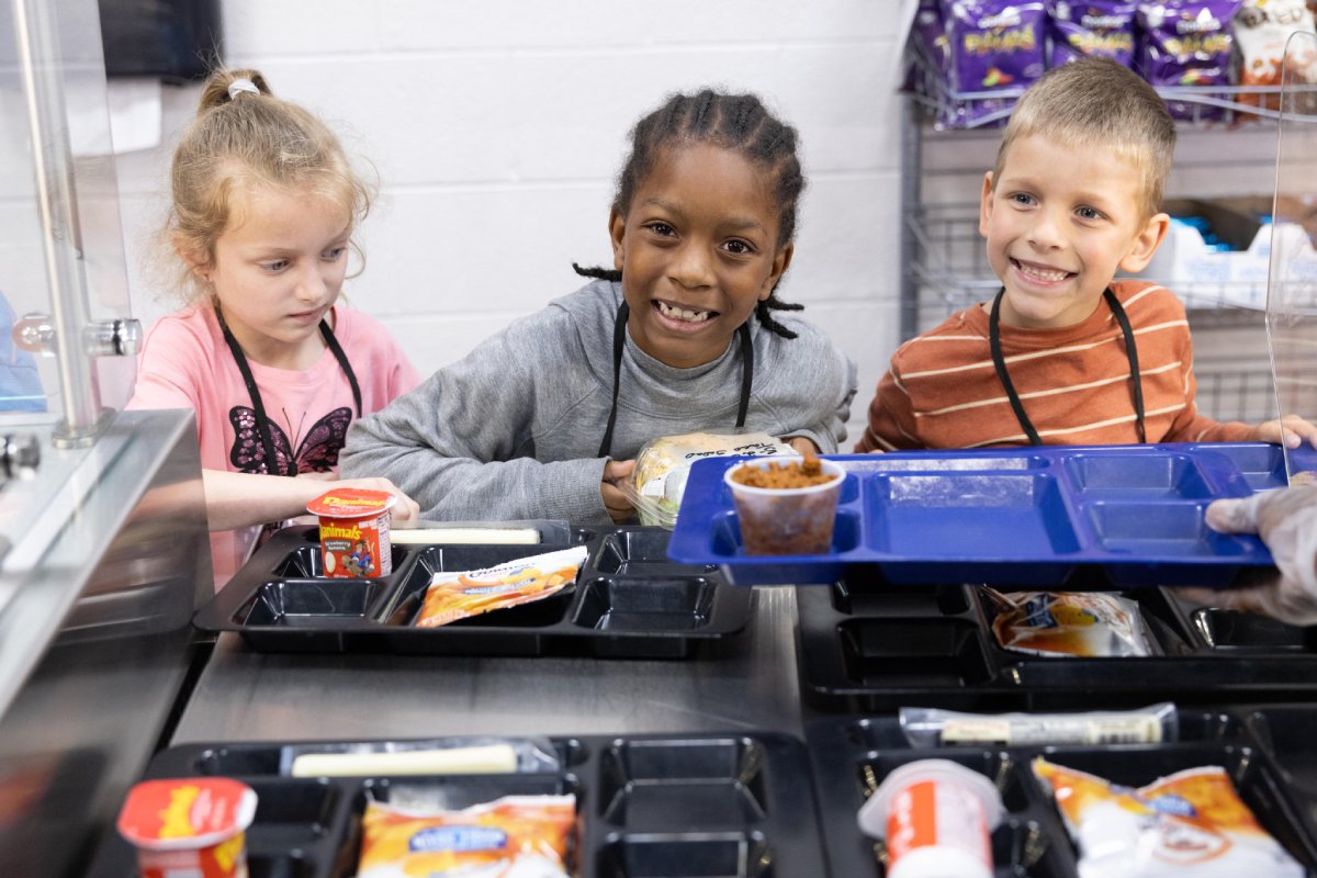 A group of children happily eating their lunch with trays of food in front of them.